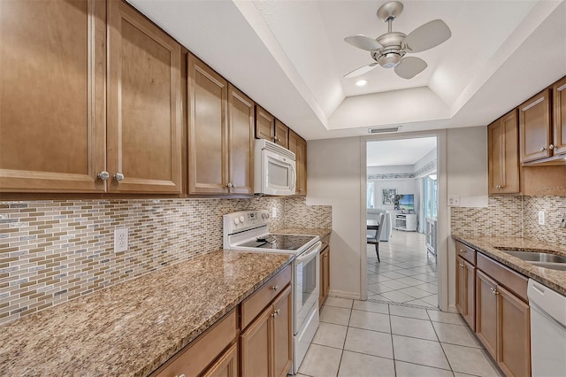 kitchen featuring white appliances, light stone countertops, a raised ceiling, light tile patterned floors, and sink