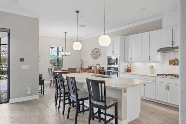 kitchen with a center island with sink, decorative light fixtures, white cabinets, and appliances with stainless steel finishes