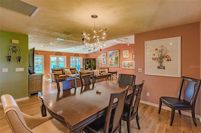 dining room with lofted ceiling, light wood-type flooring, and a notable chandelier