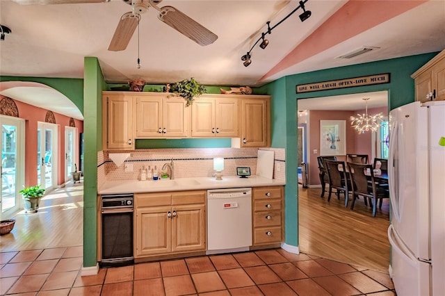 kitchen featuring lofted ceiling, backsplash, sink, white appliances, and ceiling fan with notable chandelier