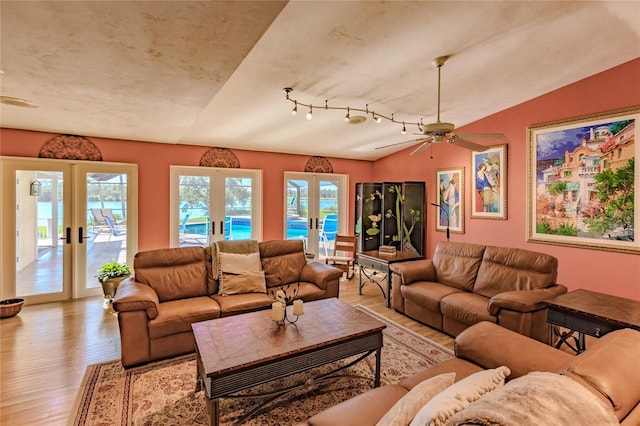 living room with ceiling fan, vaulted ceiling, a healthy amount of sunlight, light wood-type flooring, and french doors