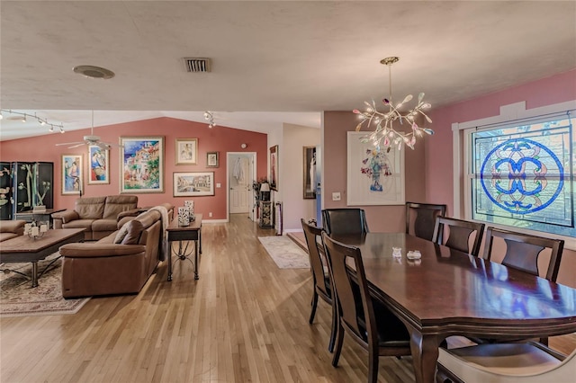 dining room featuring lofted ceiling, rail lighting, ceiling fan with notable chandelier, and light hardwood / wood-style flooring