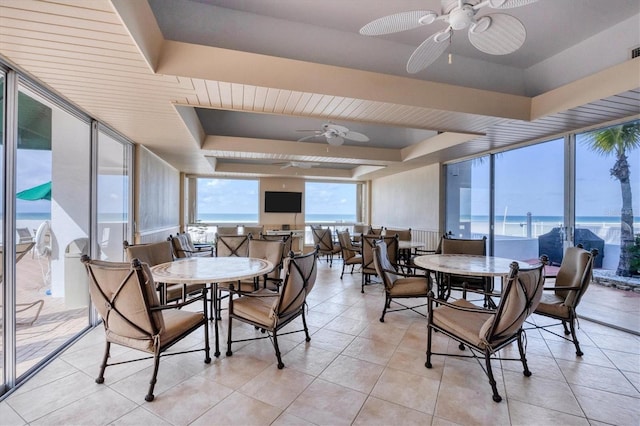 tiled dining area with ceiling fan, plenty of natural light, a raised ceiling, and expansive windows