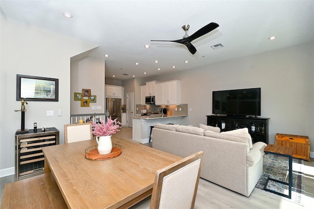 dining space featuring ceiling fan, wine cooler, and light hardwood / wood-style flooring