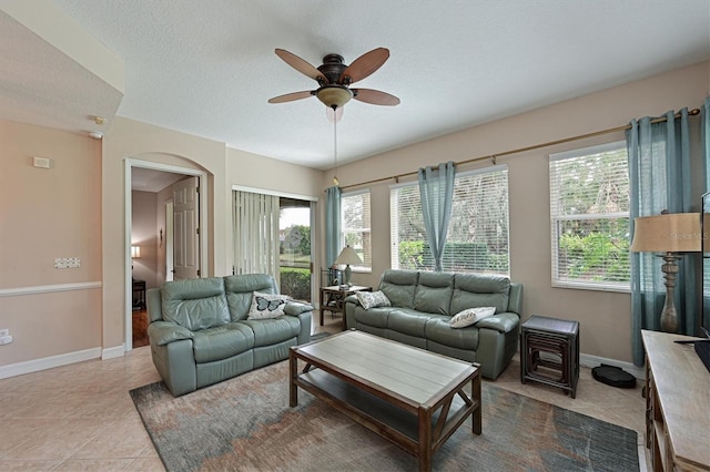 living area featuring tile patterned flooring, baseboards, arched walkways, a textured ceiling, and a ceiling fan