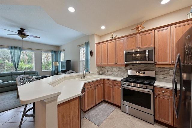 kitchen with kitchen peninsula, stainless steel appliances, a breakfast bar, backsplash, and sink