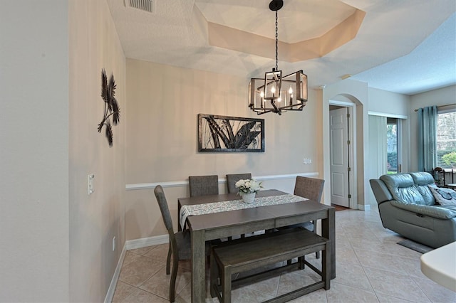 tiled dining room featuring a textured ceiling, a tray ceiling, and a chandelier