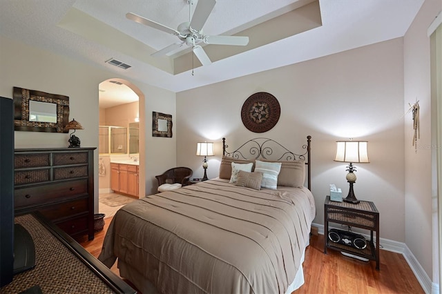 bedroom featuring a raised ceiling, arched walkways, visible vents, and light wood finished floors