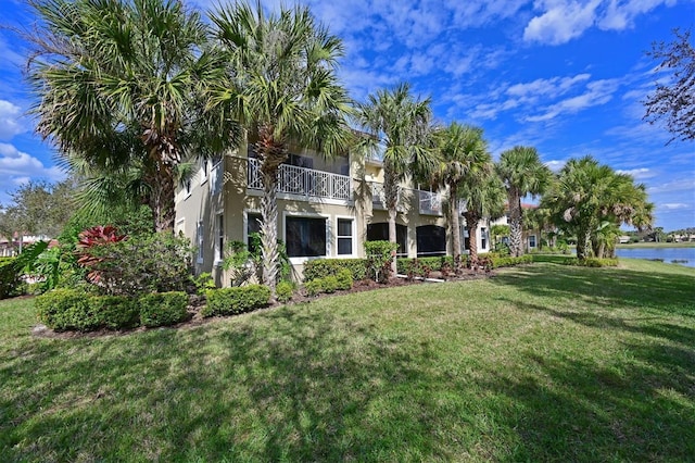 rear view of property with stucco siding, a lawn, a balcony, and a water view