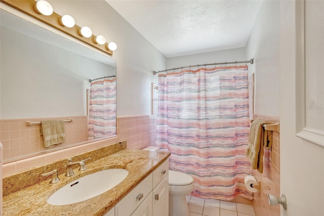 bathroom featuring a textured ceiling, tile patterned flooring, tile walls, toilet, and vanity