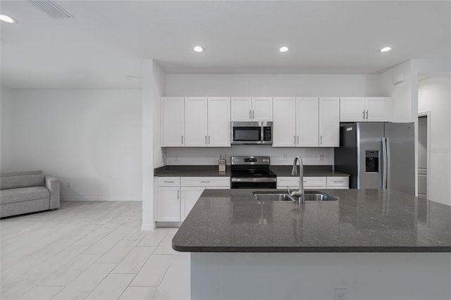 kitchen featuring stainless steel appliances, sink, white cabinetry, dark stone countertops, and a center island with sink