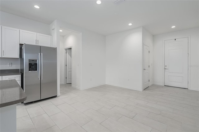 kitchen with stainless steel fridge with ice dispenser, dark stone countertops, and white cabinetry