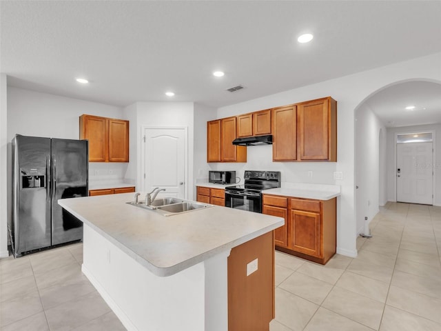 kitchen with sink, light tile patterned floors, black appliances, and an island with sink