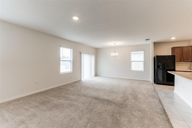 unfurnished living room with an inviting chandelier, a textured ceiling, and light colored carpet