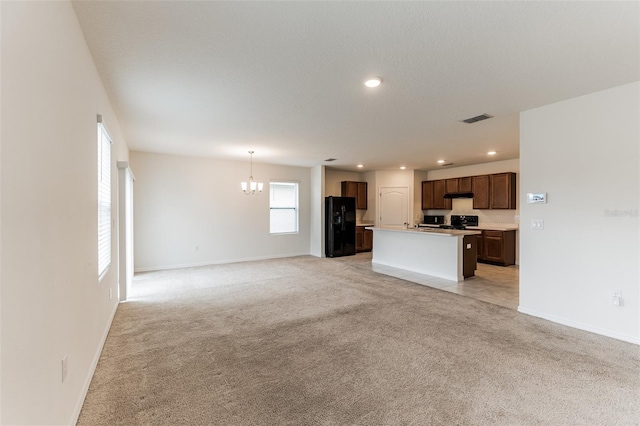 unfurnished living room featuring an inviting chandelier, light carpet, and plenty of natural light