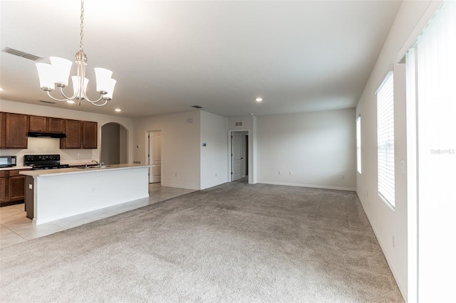 kitchen featuring decorative light fixtures, a kitchen island with sink, black appliances, and light colored carpet