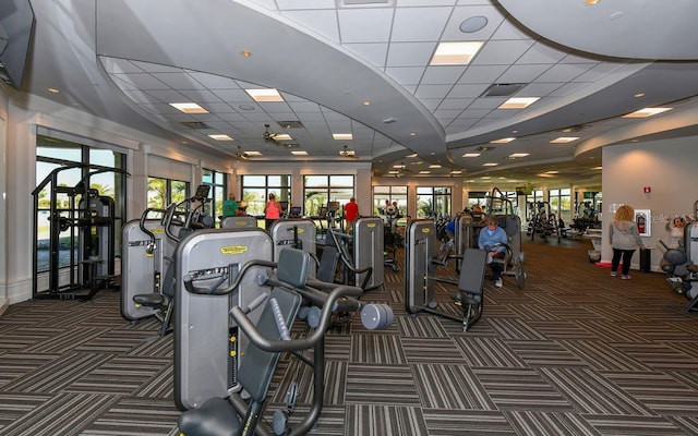 exercise room featuring a paneled ceiling and dark colored carpet