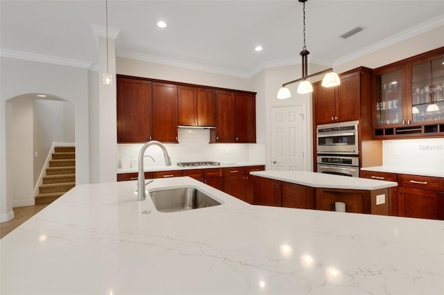 kitchen featuring appliances with stainless steel finishes, sink, hanging light fixtures, ornamental molding, and a kitchen island with sink