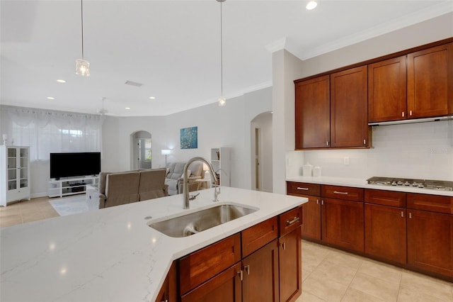 kitchen featuring stainless steel gas stovetop, backsplash, decorative light fixtures, light stone counters, and sink