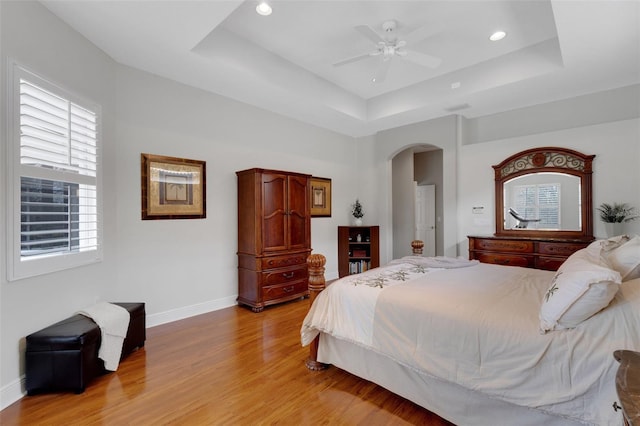 bedroom with ceiling fan, light wood-type flooring, and a tray ceiling