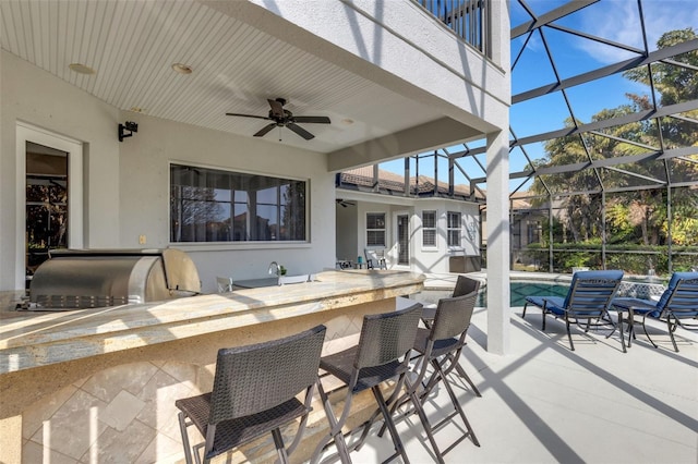 view of patio featuring ceiling fan, glass enclosure, area for grilling, and exterior bar