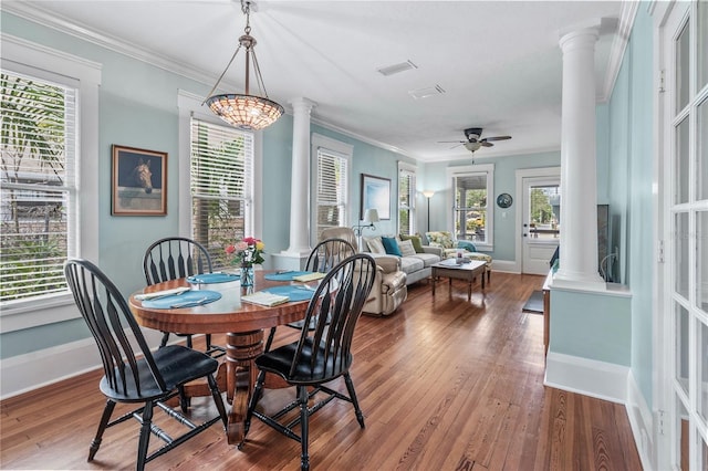 dining space with ceiling fan with notable chandelier, hardwood / wood-style flooring, ornamental molding, and ornate columns