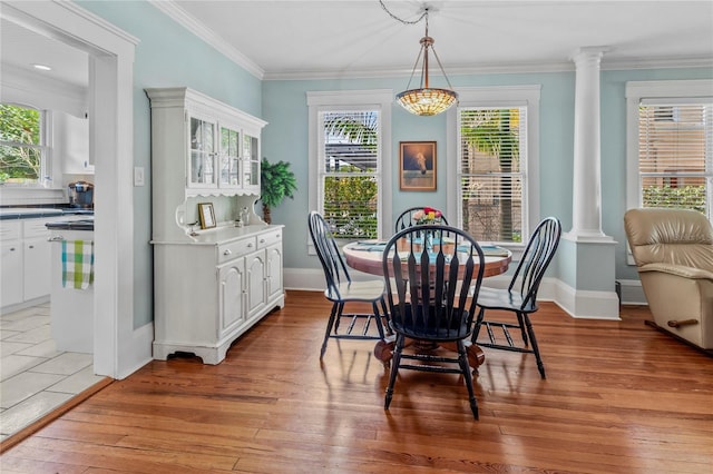 dining space featuring light wood-type flooring, ornamental molding, and ornate columns