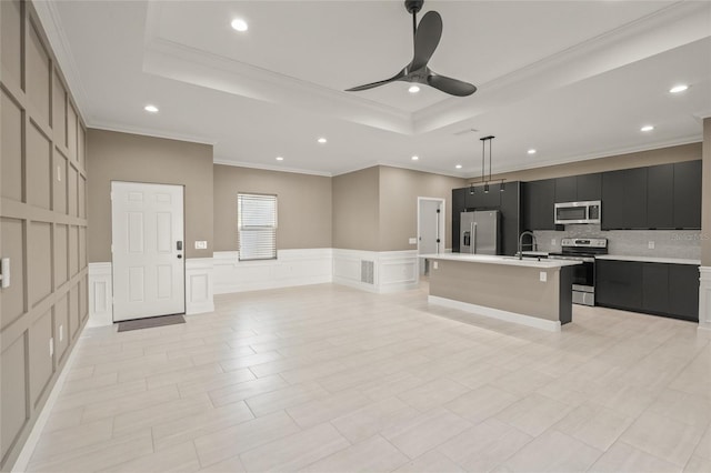 kitchen with stainless steel appliances, decorative light fixtures, a tray ceiling, and an island with sink