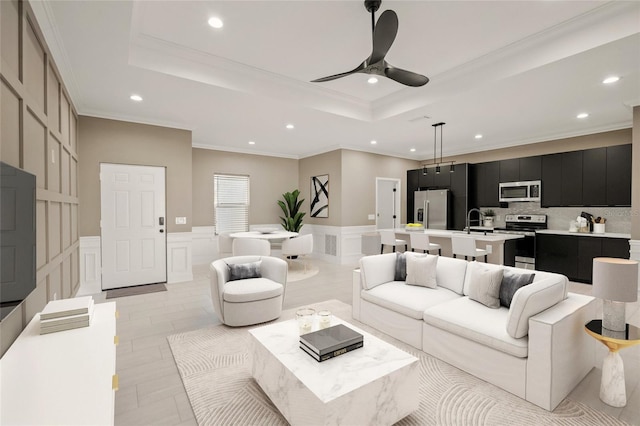 living room featuring a raised ceiling, ceiling fan, crown molding, and sink