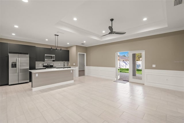 kitchen with a kitchen island with sink, a raised ceiling, stainless steel appliances, ceiling fan, and decorative light fixtures