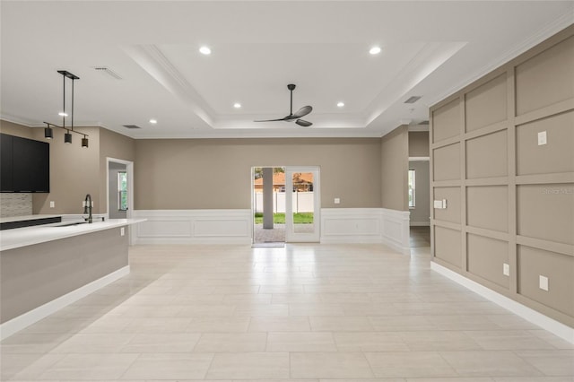 unfurnished living room featuring sink, ceiling fan, ornamental molding, and a tray ceiling