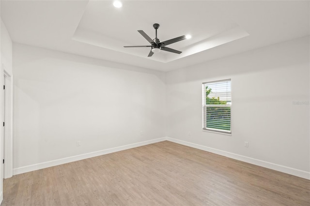 spare room with ceiling fan, light hardwood / wood-style floors, and a tray ceiling