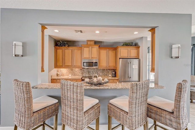 kitchen with stainless steel appliances, visible vents, a kitchen breakfast bar, backsplash, and light stone countertops