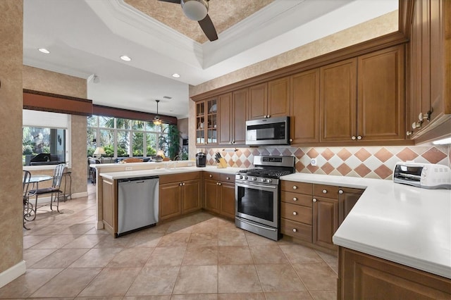 kitchen with tasteful backsplash, hanging light fixtures, ornamental molding, appliances with stainless steel finishes, and a raised ceiling