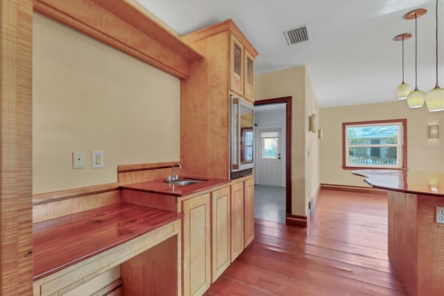 kitchen featuring light brown cabinetry, sink, light hardwood / wood-style flooring, and decorative light fixtures