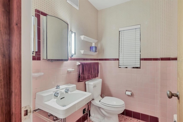 bathroom featuring toilet, tile walls, and sink