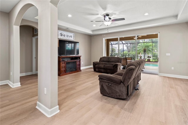 living room featuring ceiling fan, light hardwood / wood-style floors, and a raised ceiling