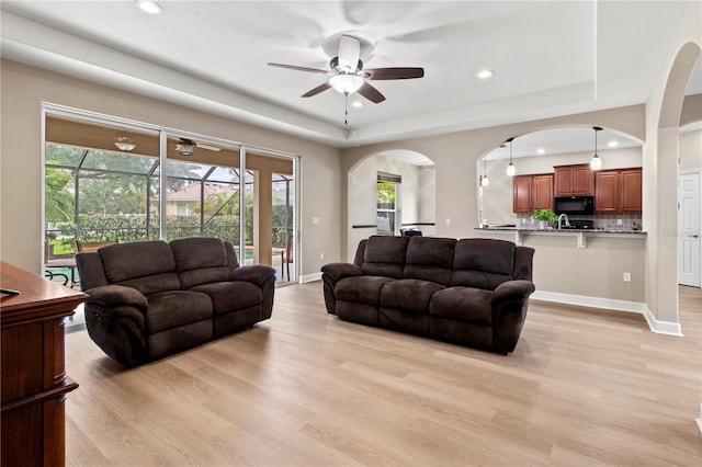 living room featuring ceiling fan, light hardwood / wood-style flooring, a raised ceiling, and sink