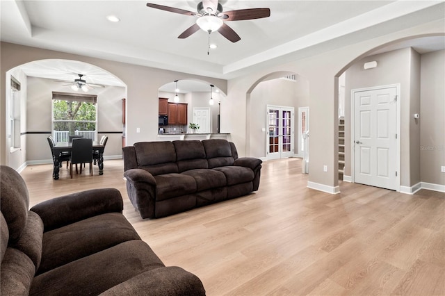 living room with ceiling fan, light hardwood / wood-style floors, and a tray ceiling