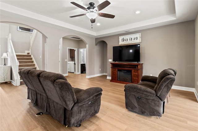 living room with ceiling fan, separate washer and dryer, a raised ceiling, and light wood-type flooring