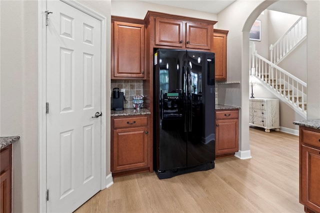 kitchen with black fridge, light wood-type flooring, and dark stone counters