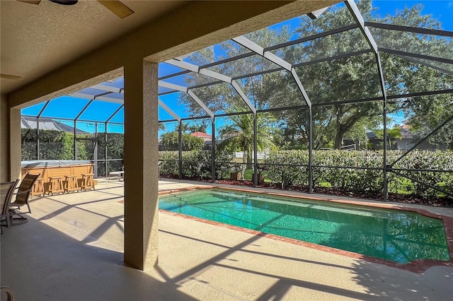 view of pool with glass enclosure, a hot tub, ceiling fan, and a patio