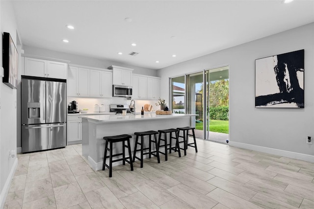 kitchen with an island with sink, white cabinetry, a kitchen bar, and stainless steel appliances