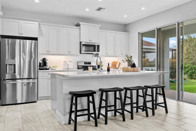 kitchen with an island with sink, white cabinetry, a breakfast bar, and appliances with stainless steel finishes