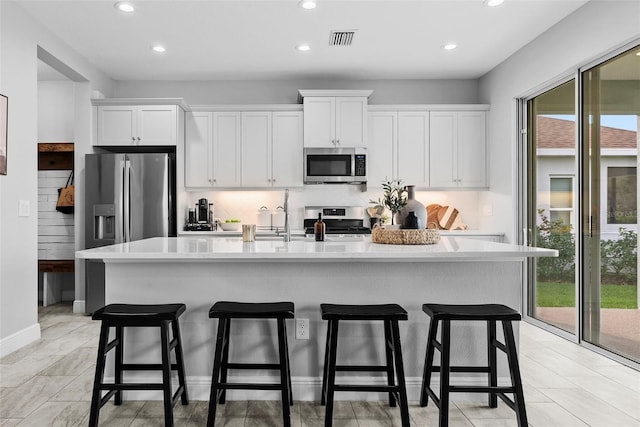 kitchen with white cabinets, a wealth of natural light, appliances with stainless steel finishes, and a center island with sink