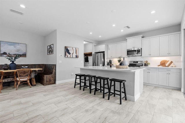 kitchen with appliances with stainless steel finishes, a kitchen bar, white cabinetry, sink, and a kitchen island with sink