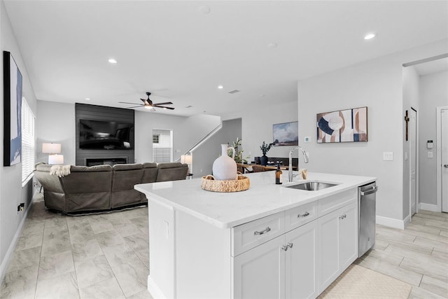 kitchen featuring white cabinets, dishwasher, a fireplace, an island with sink, and sink