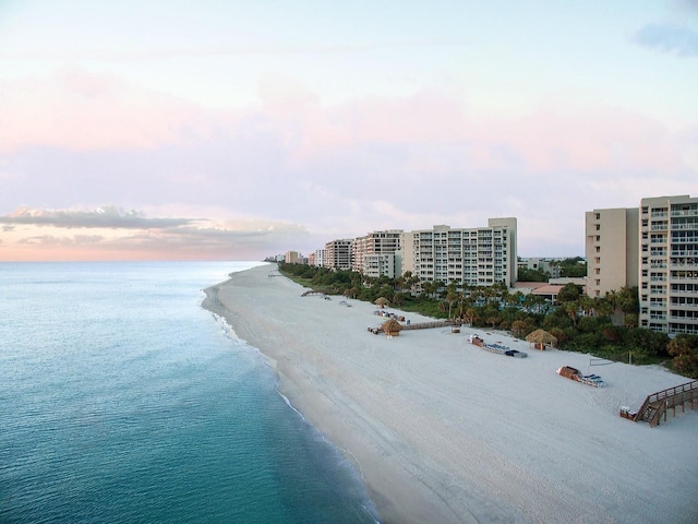 aerial view at dusk featuring a water view and a beach view