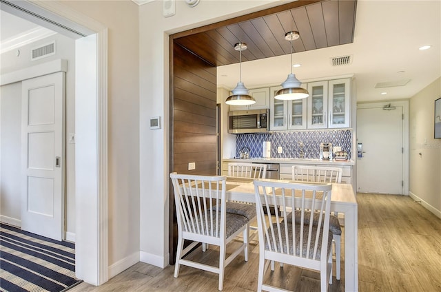 kitchen with tasteful backsplash, light wood-type flooring, stainless steel appliances, and pendant lighting