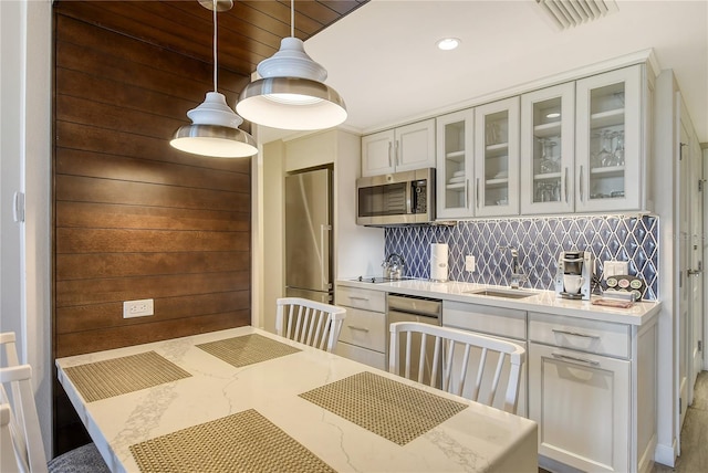 kitchen featuring white cabinetry, wood walls, stainless steel appliances, decorative light fixtures, and sink